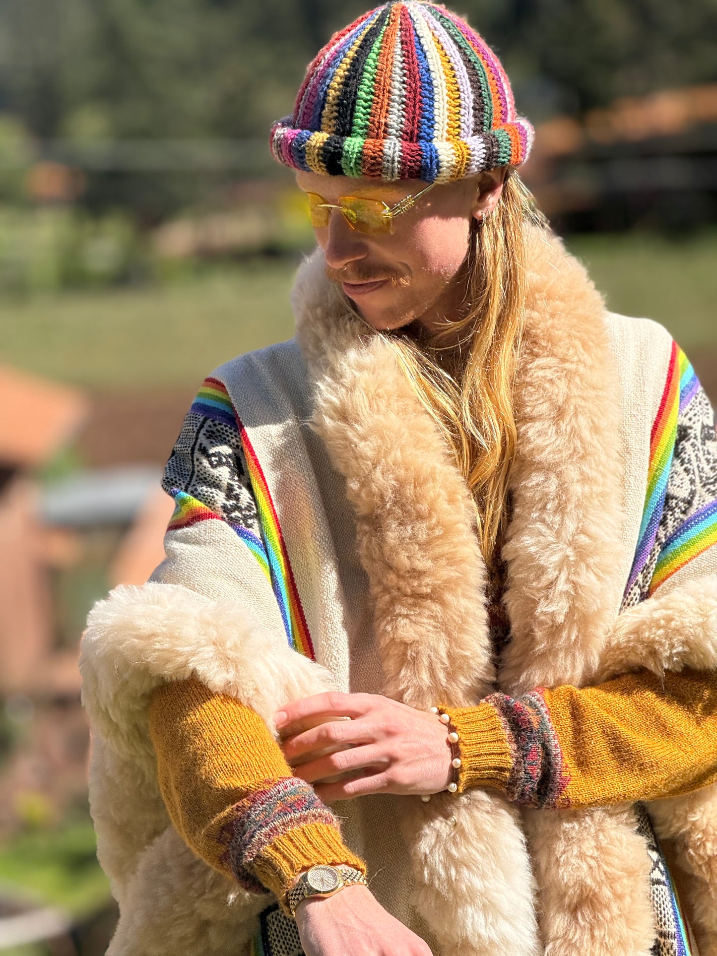 Person wearing a colorful knit hat and coat with a rainbow pattern, standing outdoors.
