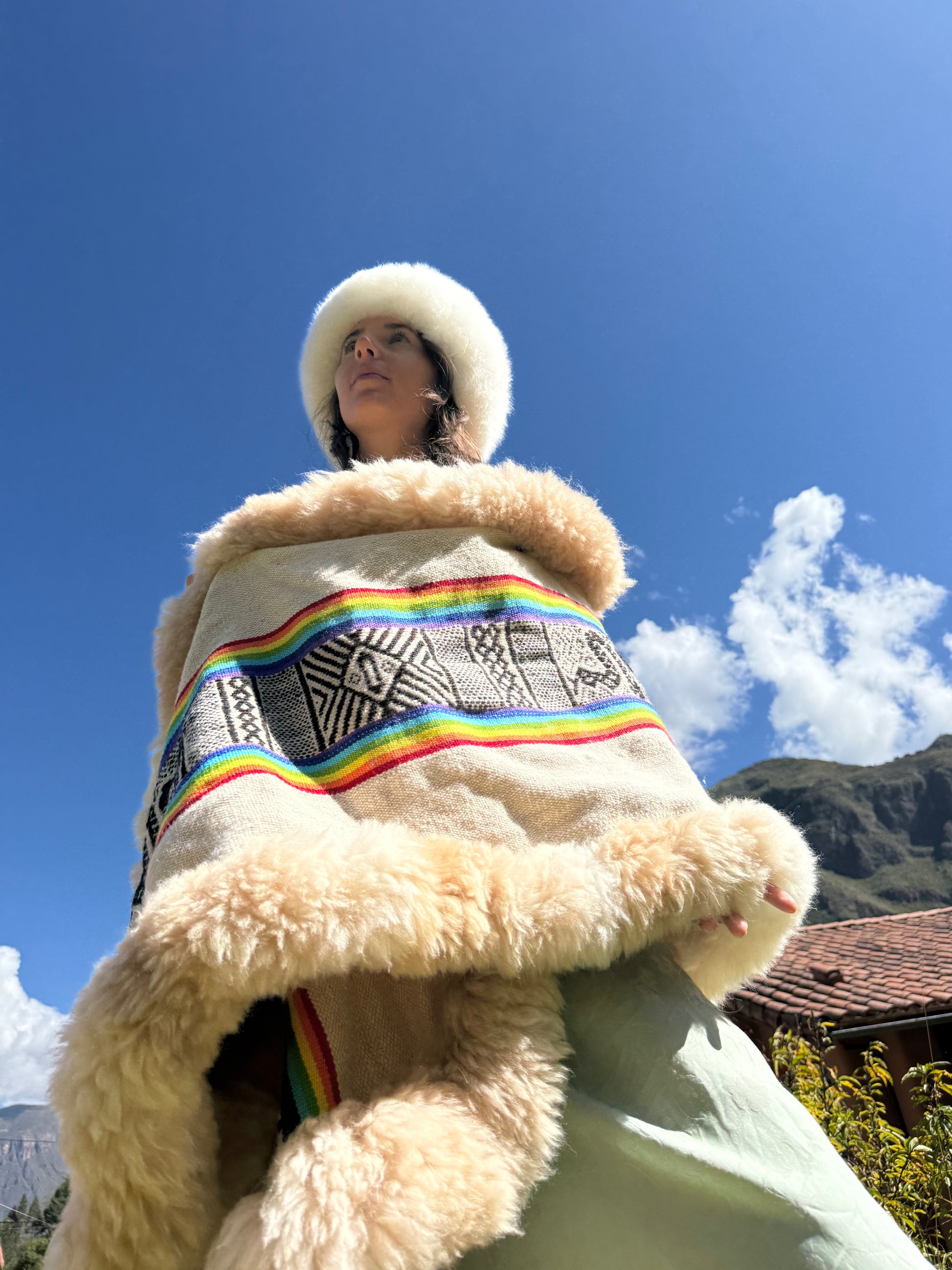 Person wearing a traditional garment with a rainbow design against a mountainous background